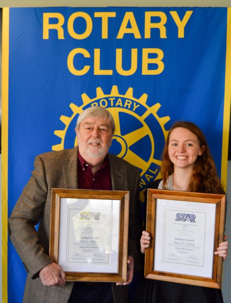 female STAR student and male STAR teacher in front of Rotary Club banner